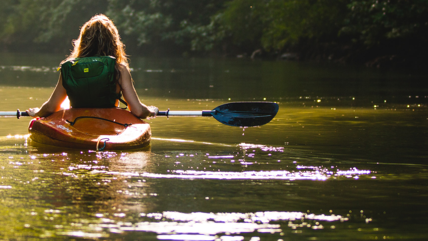 Woman paddling a kayak on smooth water.