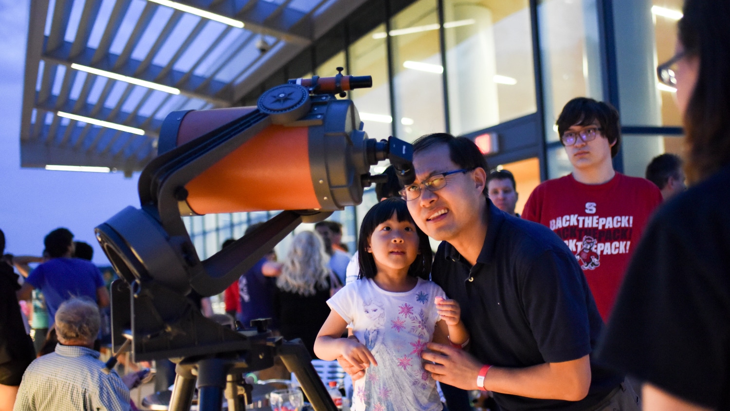 A man and his daughter look through a telescope at a College of Sciences event at Hunt Library.