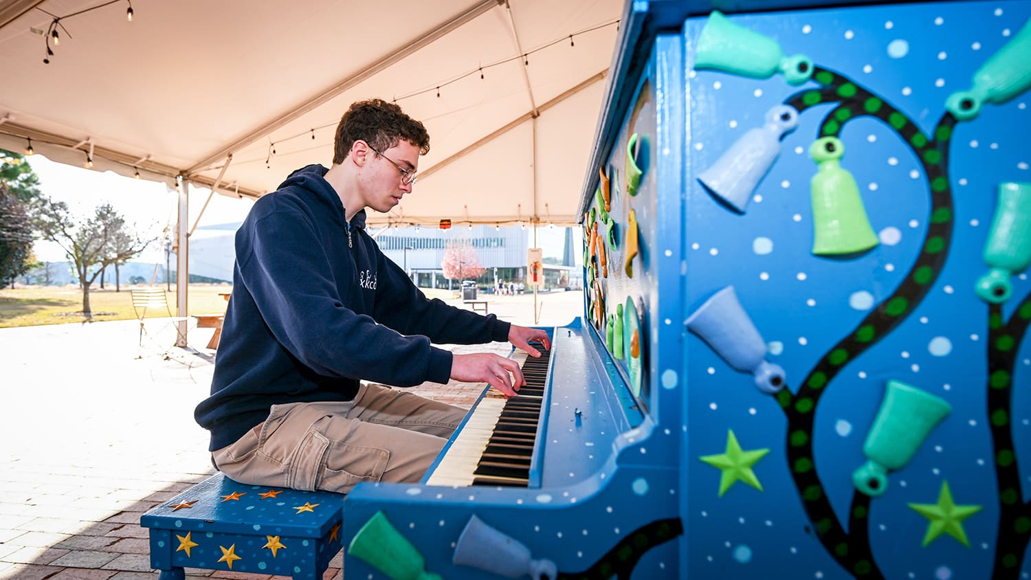 A student plays a piano painted with a colorful blue mural.
