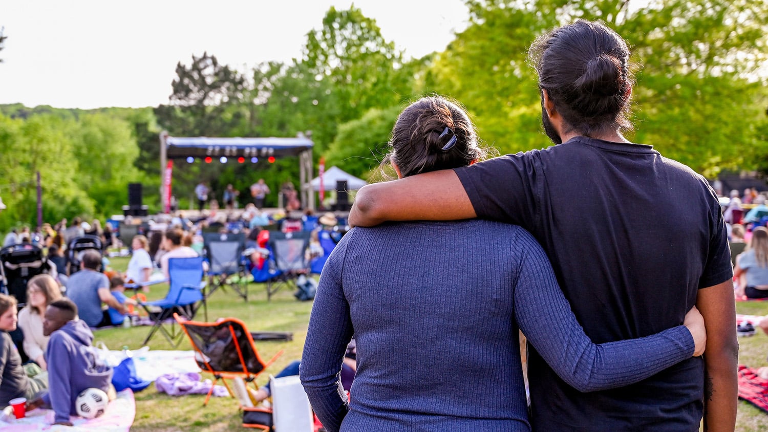 An all-ages crowd watches as a folk band performs on a stage near Lake Raleigh.