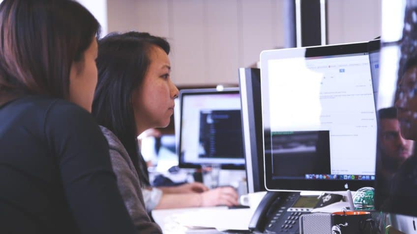 Two young professionals collaborate on a desktop computer.